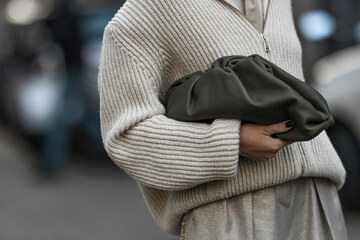 kobieta w beżowym rozpinanym swetrze z czarną torebką w ręce