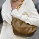 kobieta w swetrowej białej sukience niesie brązową torbę na ramieniu, torba jest na złotym łańcuchu